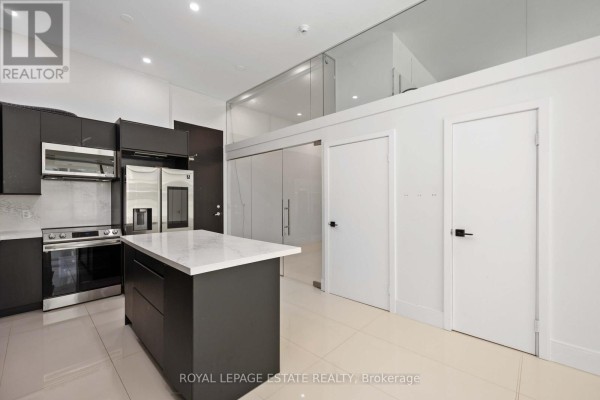 Kitchen with dark cabinetry, stainless steel appliances, island, and glass partition to upper loft. - 127 - 637 Lake Shore Boulevard W, Toronto