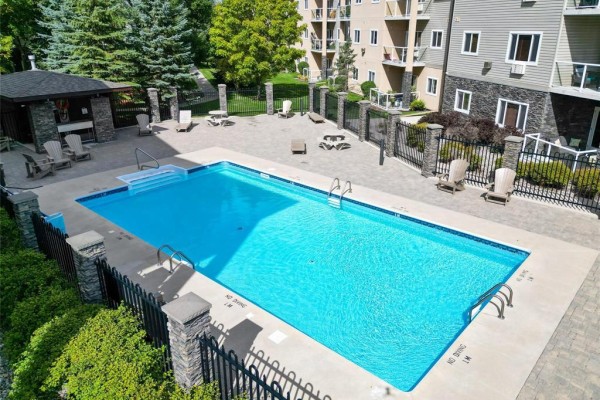 Outdoor swimming pool with lounge chairs, umbrellas, and building in background. - 127 230 Fairhaven Road, Winnipeg