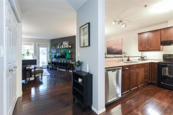 Open concept living room and kitchen with dark wood floors and stainless steel appliances. - 127 230 Fairhaven Road, Winnipeg