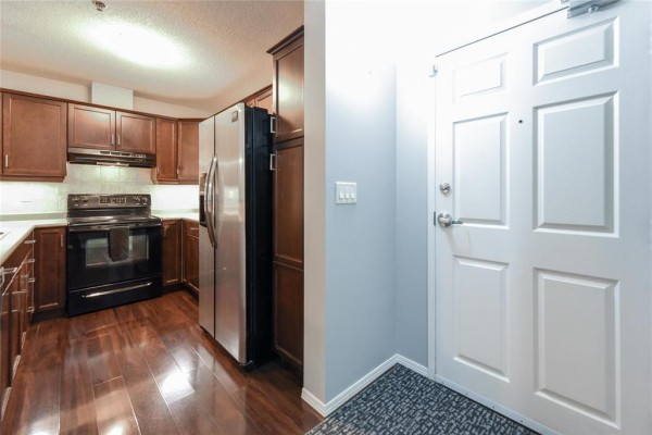 Kitchen with dark wood cabinets, stainless steel appliances, and dark wood floors. - 127 230 Fairhaven Road, Winnipeg