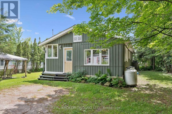 Side view of the green mobile home showing the entrance and surrounding natural landscape. - 127 Cedar Crescent, Centre Wellington