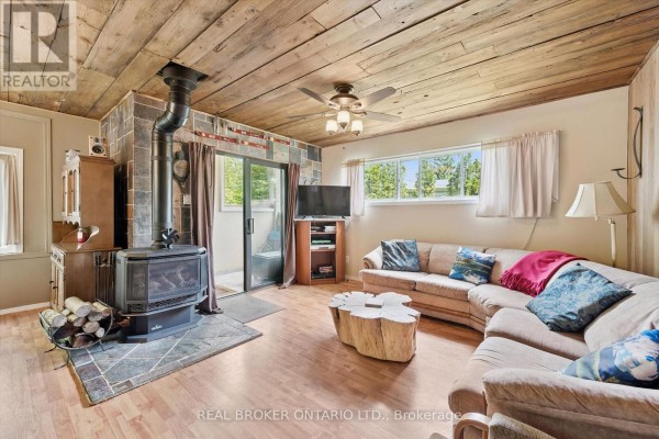 Living room with a wood-burning stove, sectional sofa, tree stump coffee table, and wood-paneled ceiling. - 127 Cedar Crescent, Centre Wellington