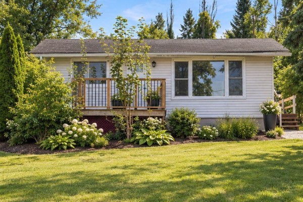 Front exterior of a white bungalow with a wooden deck and green lawn. - 127 Coleman Crescent, Scugog