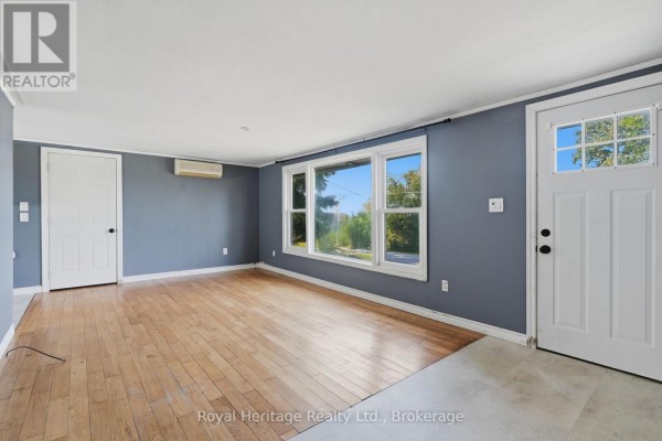 Living room with hardwood floors, a wide window, a white door, and grey walls. - 127 Coleman Crescent, Scugog
