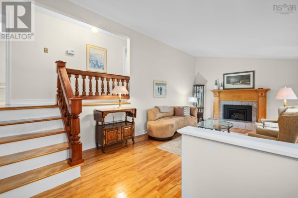 Living room with hardwood floors, fireplace, wooden staircase, and tan sofa. - 127 Evans Avenue, Halifax