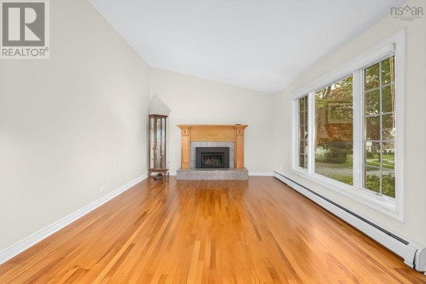 Empty living room with hardwood floors, fireplace, and a large bay window with natural light. - 127 Evans Avenue, Halifax