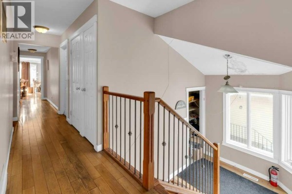 Interior hallway with wood flooring, white doors, and a staircase with a metal railing. - 127 Scenic Cove Circle Nw, Calgary