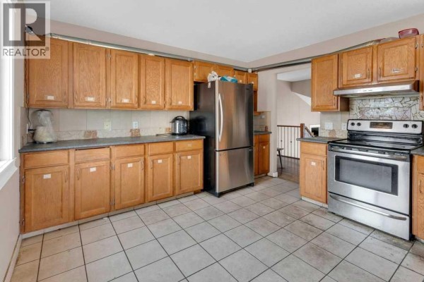 Kitchen with light wood cabinets, stainless steel appliances, tile flooring, and a large refrigerator. - 127 Scenic Cove Circle Nw, Calgary