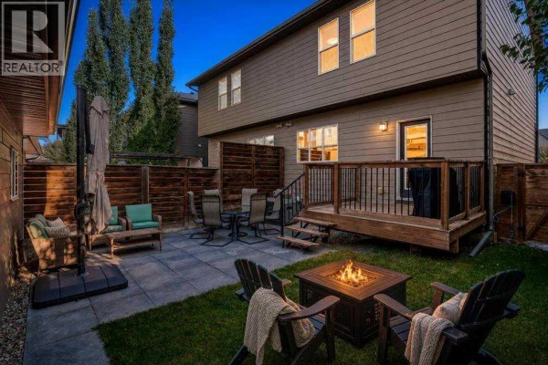 Backyard with a wooden deck, stone patio, outdoor furniture, fire pit, and privacy fencing. - 1270 Walden Drive Se, Calgary