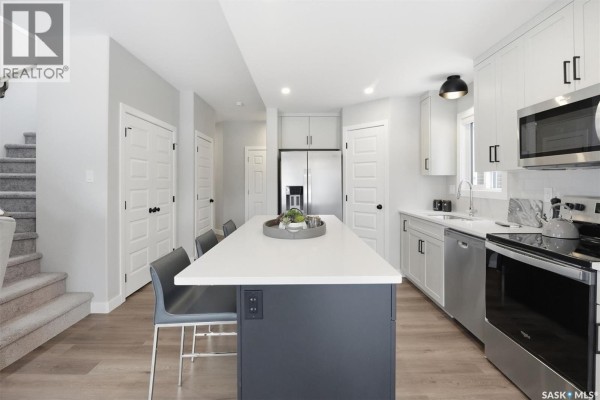 Modern kitchen with stainless steel appliances, white quartz countertops, and a large island with seating. - 1270 Yuel Way, Saskatoon