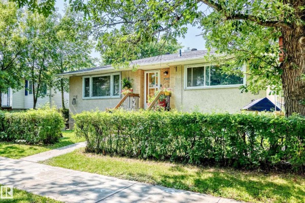 Side exterior view of the duplex showing the entryway and surrounding green foliage. - 12718 126 St Nw, Edmonton