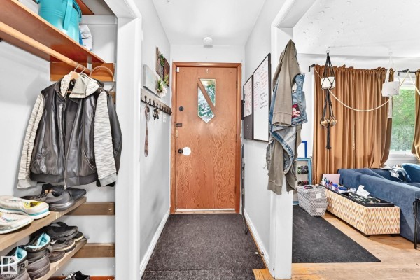 Interior entryway with a wooden door, coat hooks, shoe shelving, and a glimpse of a living area. - 12718 126 St Nw, Edmonton