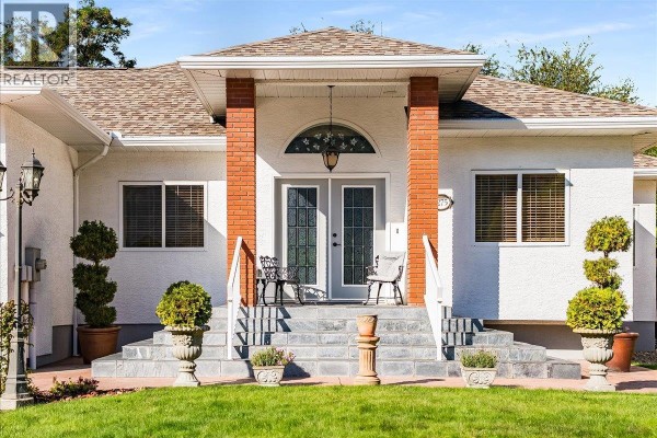 Close-up of the home's entrance featuring double glass doors, brick pillars, and stone steps. - 1275 Paquette Drive, Trail