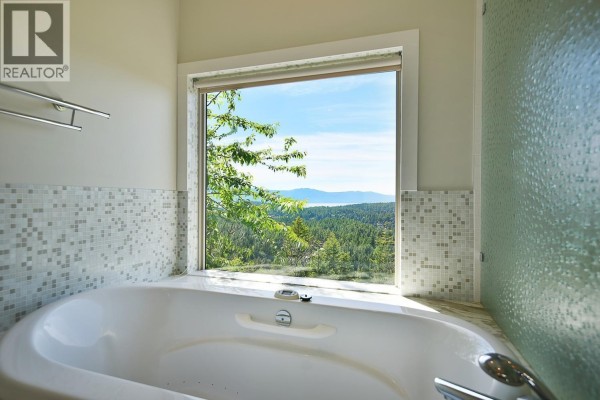 Corner bathtub with a large window overlooking a forested landscape and distant water and mountains. - 12753 Gulfview Road, Madeira Park