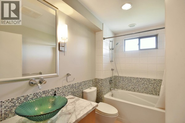Bathroom with bathtub, toilet, vanity with green glass bowl sink, and tiled accent walls. - 12753 Gulfview Road, Madeira Park