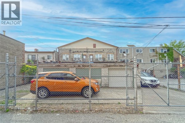 View of property garages and paved area behind a chain-link fence with two cars. - 1276-1282 Wyandotte Street East, Windsor