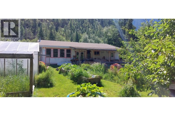 Rear view of house under renovation with greenhouse, garden beds, wooded area behind. - 1276 Mackenzie Highway, Bella Coola