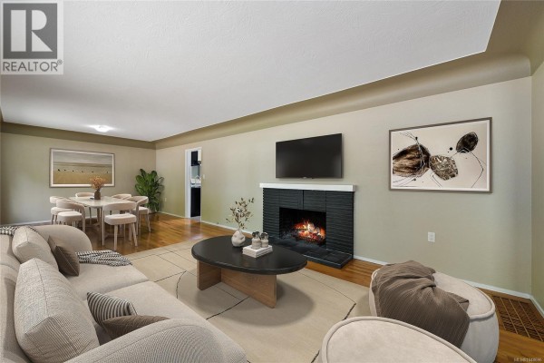 Living room with a sectional sofa, coffee table, fireplace, and dining area visible in the background. - 1277 Revercomb Pl, Victoria