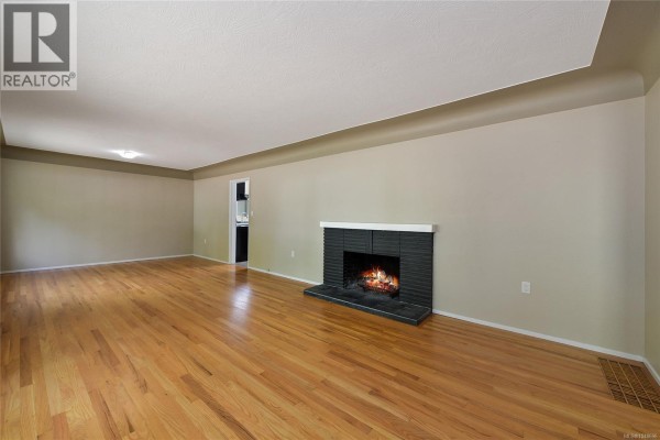 Empty living room with polished hardwood floors and a black brick fireplace with a white surround. - 1277 Revercomb Pl, Victoria