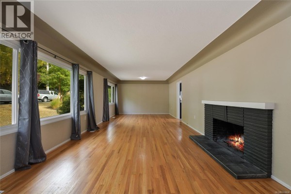Living room with large windows showing a street view, hardwood floors, and a fireplace. - 1277 Revercomb Pl, Victoria