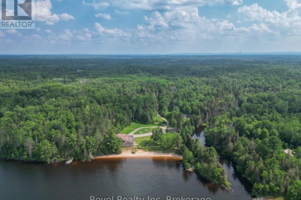 Aerial view of a sprawling property surrounded by dense green forest, featuring a small beach and a body of water. - 1278 Highway 654 Highway W, Callander