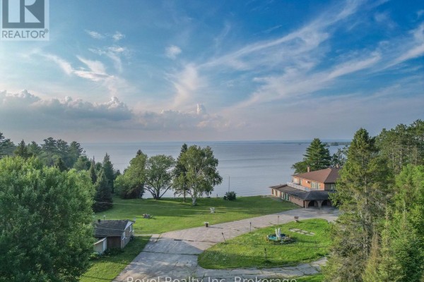 Aerial view of a waterfront property with a house, green lawns, paved driveway, and mature trees under a partly cloudy sky. - 1278 Highway 654 Highway W, Callander