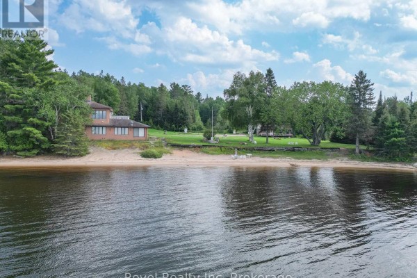 View from the water of a brick house with a sandy beach in front and surrounded by lush green trees. - 1278 Highway 654 Highway W, Callander