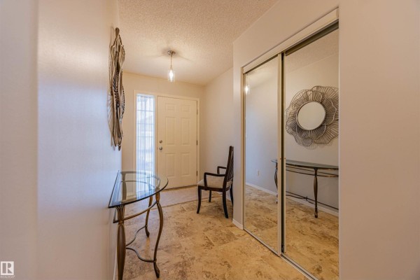 Interior view of a duplex entryway with tiled floors, mirrored closet doors, and a chair. - #128 215 Blackburn East Dr Sw, Edmonton
