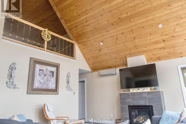 Living room with vaulted wood ceiling, fireplace with grey tile surround, and a wall-mounted television. - 128 Bayview Drive, Greater Napanee