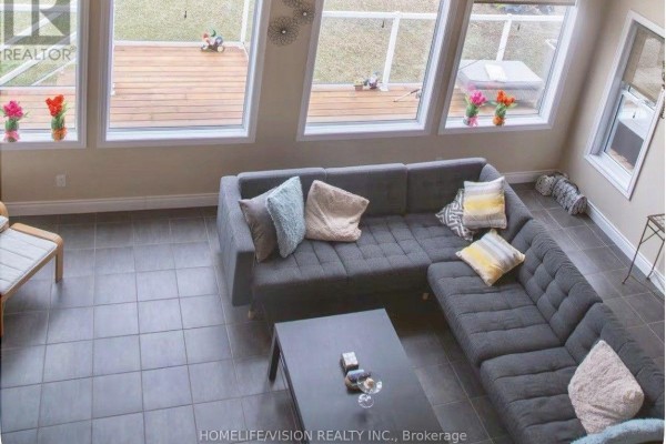 View from above of a grey sectional sofa in a living room with large windows and tile flooring. - 128 Bayview Drive, Greater Napanee
