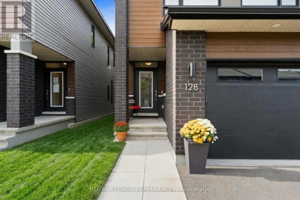 Close-up of the front entrance with a glass-paned door, dark brickwork, and a large black garage door on the right. - 128 Bristol Crescent, North Grenville