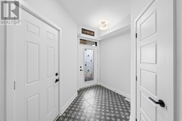 Interior foyer with white walls, patterned black and white floor tiles, a decorative glass front door, and white panel doors. - 128 Bristol Crescent, North Grenville