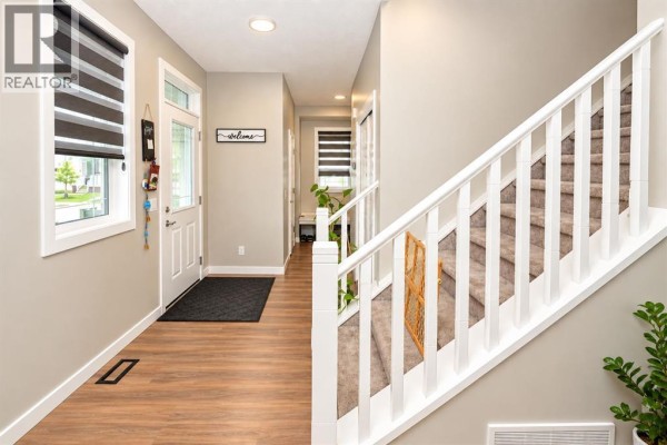 Interior view of a home's entrance with a staircase and wood-look flooring. - 128 Cityside Crescent Ne, Calgary