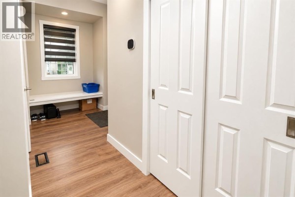 Interior view of a mudroom area with sliding doors, a bench, and wood-look flooring. - 128 Cityside Crescent Ne, Calgary