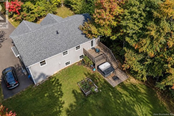 Rear aerial view of the grey house, showing a wooden deck, hot tub, and garden bed. - 128 Country Wood Lane, Richibucto Road