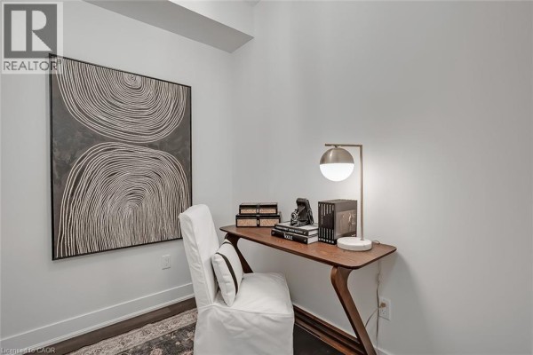 A small home office setup with a wooden desk, a white chair, and abstract art on the wall. - 128 Garden Drive Unit# 102, Oakville