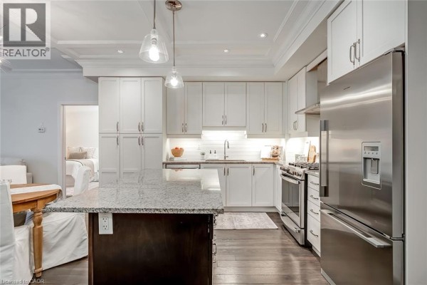 Kitchen view showing white cabinets, stainless steel appliances, and a granite-top island. - 128 Garden Drive Unit# 102, Oakville