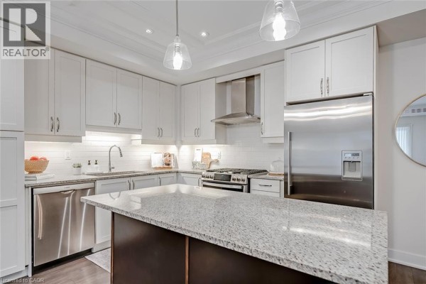 View of the kitchen island with granite countertop, white cabinets, and stainless steel appliances. - 128 Garden Drive Unit# 102, Oakville