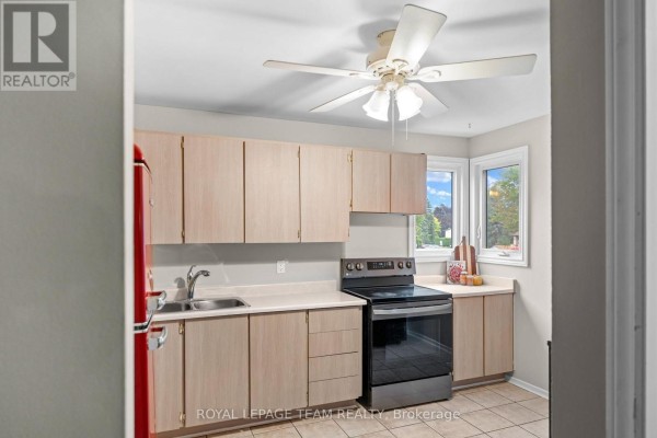Kitchen with light wood cabinets, a black stove, double sink, and tiled floor. - 128 Mcclintock Way, Ottawa