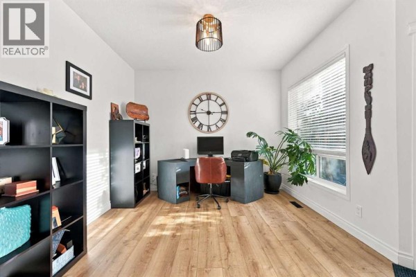 Interior view of a home office with a desk, shelves, a large clock, and plants. - 128 Seagreen Way, Chestermere