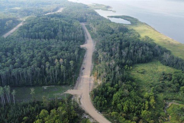 Aerial view looking down a winding dirt road through a dense forest with a lake visible in the distance. - 128 Sunset Drive, Lake Of The Prairies