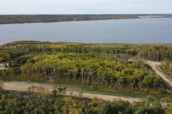 Overhead view of a forested landscape with a winding road and a wide lake under a cloudy sky. - 128 Sunset Drive, Lake Of The Prairies