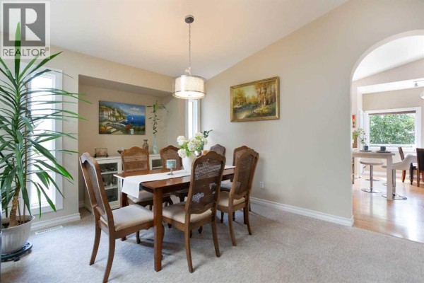 Formal dining room with wooden table and chairs, carpeted floor, and an archway to the kitchen. - 128 Waterstone Place Se, Airdrie