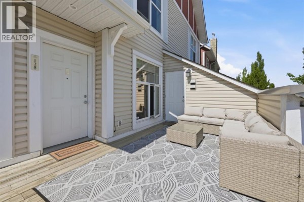 Townhouse entrance with beige siding, two white doors, and a patio with outdoor furniture. - 128 West Springs Road Sw, Calgary