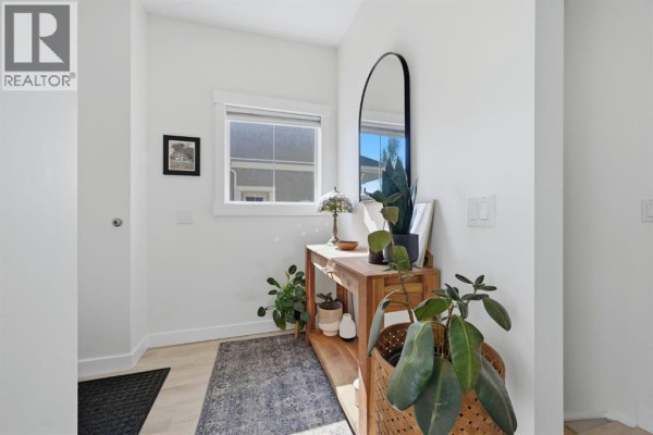 Interior entryway with light wood floors, a console table with plants, and a large mirror. - 128 West Springs Road Sw, Calgary