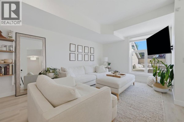 Bright living room with white furniture, a large mirror, and a view of an outdoor patio. - 128 West Springs Road Sw, Calgary