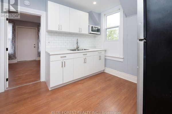 Kitchen with white cabinets, subway tile backsplash, double sink, and laminate flooring. - 128 West Street, Chatham Kent