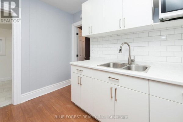 View of the kitchen from the side, showing white cabinets, sink, and doorway to another room. - 128 West Street, Chatham Kent