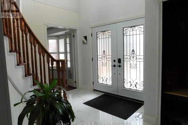 Interior foyer with a staircase, double glass doors with ornate metal detailing, and a large potted plant. - 128 William Stephenson Drive, Whitby