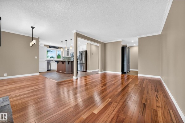 Living room with hardwood floors, stone fireplace, and large windows overlooking the exterior. - 12819 45 St Nw, Edmonton